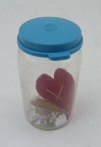 Glas mit 12 Wachsstücken in Staniolpapier und zwei ausgeschnitte Herzen aus Leder