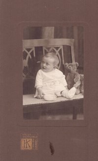 Foto Kleinkind mit Teddy auf einer Bank sitzend.