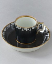 Tasse mit Unterteller mit Blütenrosetten auf schwarzem Grund